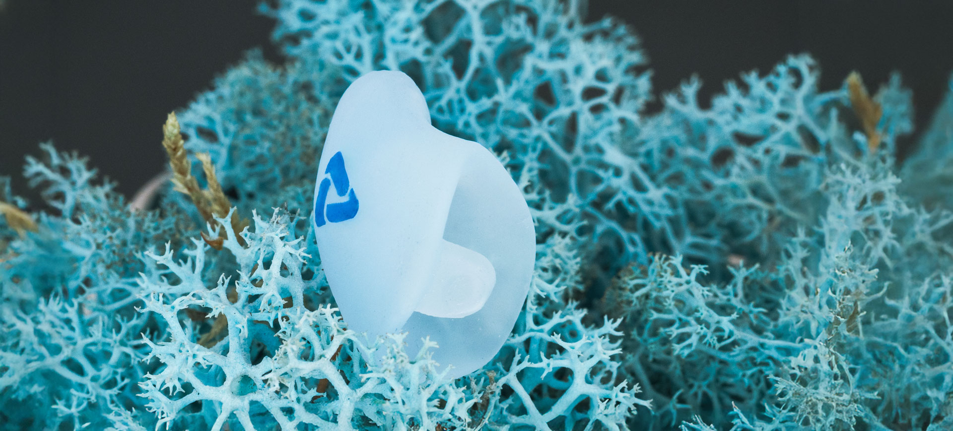 Maßgefertigte PROTECT-Otoplastik von myEarmold für Hörsysteme auf blauem 3D-Strukturhintergrund